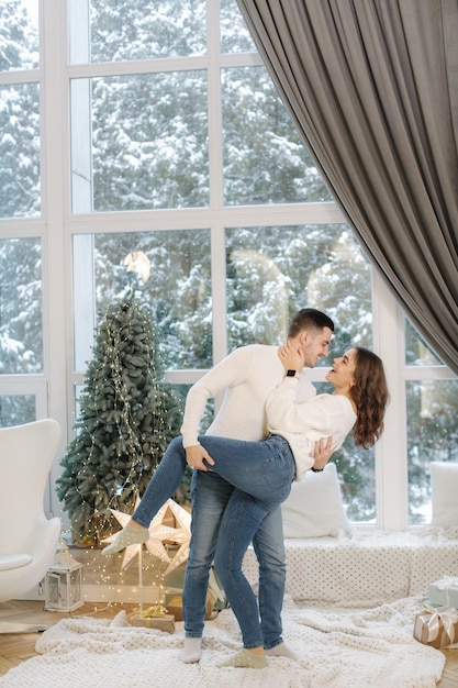 Hermosa joven pareja posando para el fotógrafo en el estudio de año nuevo fuera de la nieve del árbol de navidad