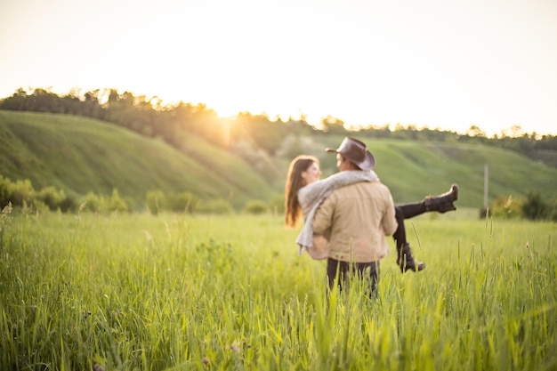 Hermosa joven pareja en un prado verde en los rayos del sol poniente un hombre sostiene a una niña en sus brazos estilo vaquero clothesrustic