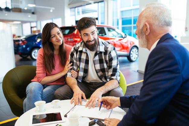 Hermosa joven pareja en la sala de exposición de coches eligiendo un coche nuevo para comprar