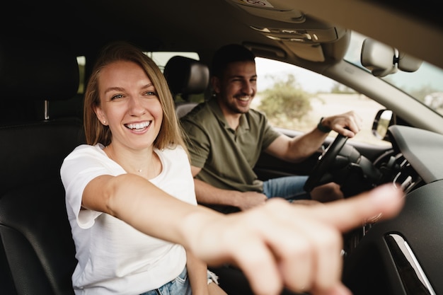 Hermosa joven pareja sentada en los asientos del pasajero delantero y conduciendo un coche