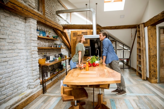 Hermosa joven pareja sonriendo mientras cocina en la cocina en casa