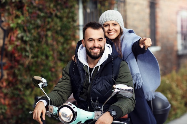 Hermosa joven pareja sonriendo mientras monta scooter en la ciudad en otoño