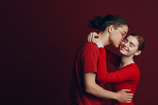 Hermosa joven pareja sonriente abrazándose sobre fondo rojo.