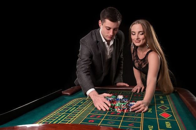 Hermosa joven pareja toma sus ganancias en la mesa de la ruleta en el casino