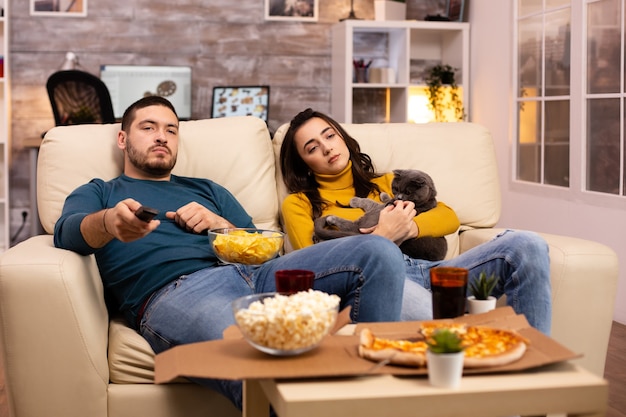 Hermosa joven pareja viendo la televisión y comiendo comida rápida para llevar en la sala de estar