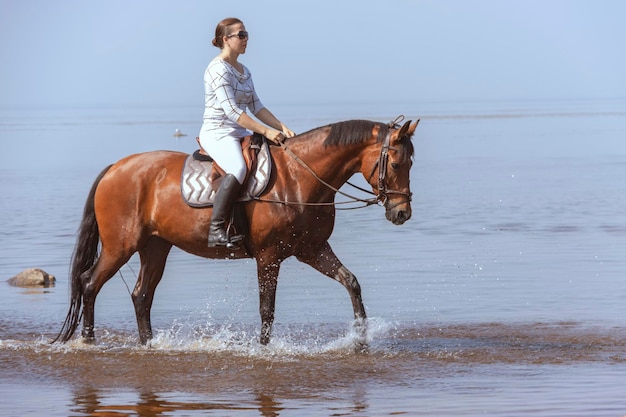 Hermosa joven en un paseo a caballo en el agua en un caluroso día de verano Entrenamiento deportivo