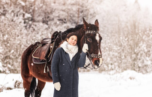 Hermosa joven en un paseo con un caballo en invierno en el bosque