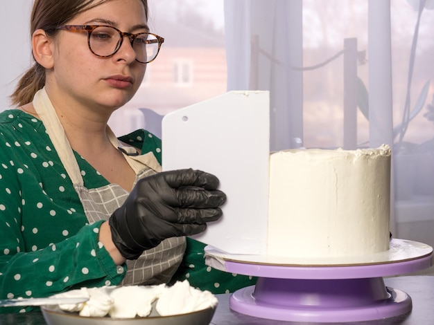 Hermosa joven pastelera hace un pastel con crema blanca usando una espátula de cocina