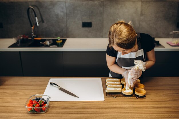 Hermosa joven pastelera prepara dulces en un fondo de cocina moderna