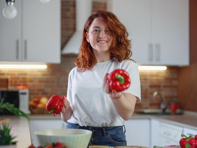 Hermosa joven pelirroja está preparando ensalada de verduras en la cocina