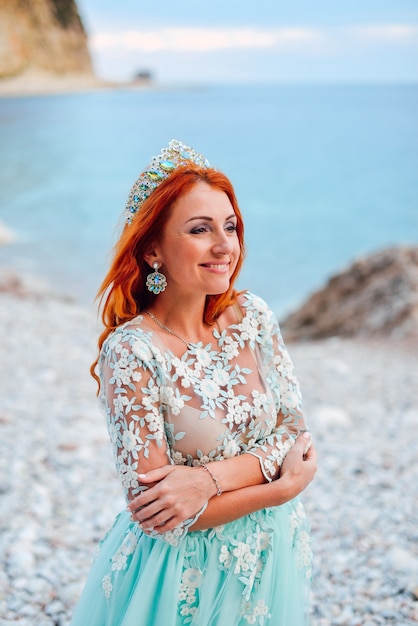 Hermosa joven pelirroja en un lujoso vestido de pie sobre una orilla rocosa del mar Adriático, primer plano