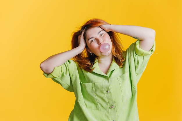 Una hermosa joven pelirroja mirando a la cámara sonriendo e inflando una bola de chicle