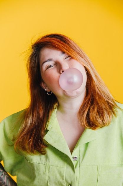 Una hermosa joven pelirroja mirando a la cámara sonriendo e inflando una bola de chicle