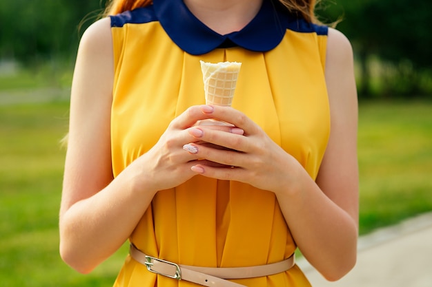 Y hermosa joven pelirroja pelirroja con un vestido amarillo comiendo helado de vainilla en un cono de galleta en el parque de verano