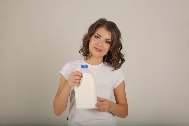 Una hermosa joven de pelo castaño con una camiseta blanca sostiene una botella de leche en sus manos