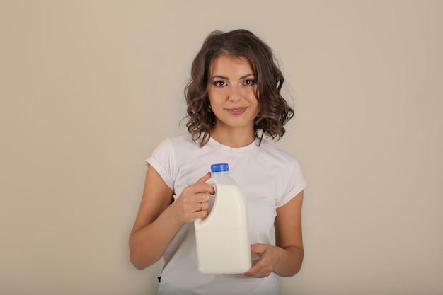 Una hermosa joven de pelo castaño con una camiseta blanca sostiene una botella de leche en sus manos