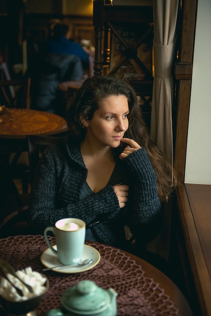 Hermosa joven de pelo castaño sentado en un café y bebiendo un capuchino.