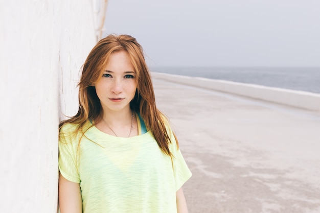 Hermosa joven con el pelo rojo mirando a la cámara en la playa