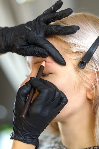 Foto hermosa joven con pestañas largas depilarse las cejas en un salón de belleza. corrección de cejas. concepto de belleza. maquillaje permanente. ceja microblading. esteticista haciendo tatuajes de cejas.