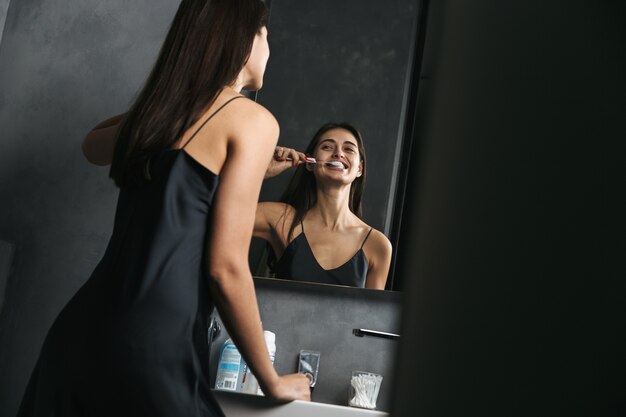 Hermosa joven de pie en el espejo en el baño por la mañana