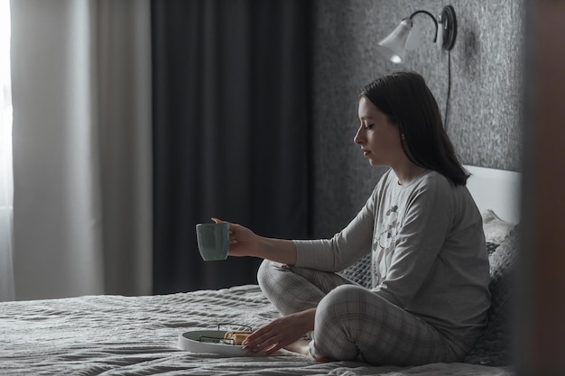 Foto una hermosa joven en pijama se sienta sola en la cama por la mañana en su dormitorio