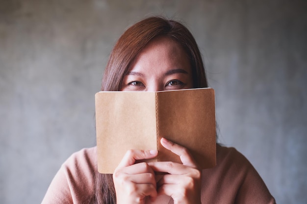 Una hermosa joven poniendo un cuaderno para cubrirse la cara