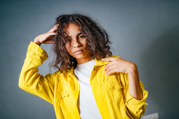 Hermosa joven posa para la cámara sobre fondo gris. Cabello rizado y chaqueta amarilla. Retrato.