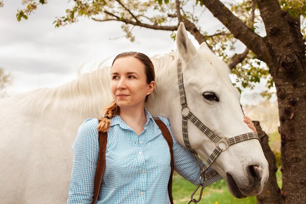 Una hermosa joven posa junto a un caballo blanco