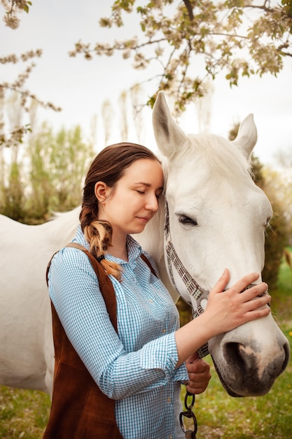 Una hermosa joven posa junto a un caballo blanco