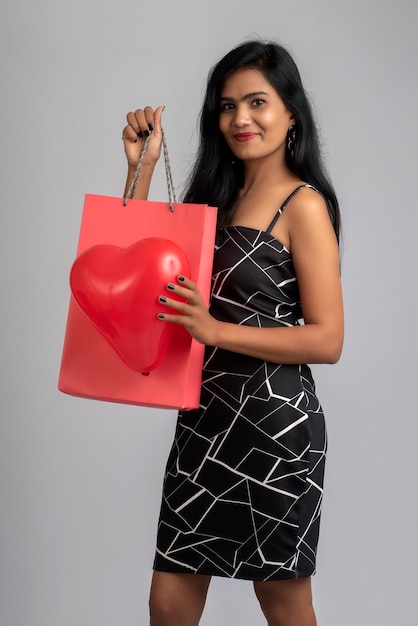 Hermosa joven posando con bolsas de la compra y globo en un gris