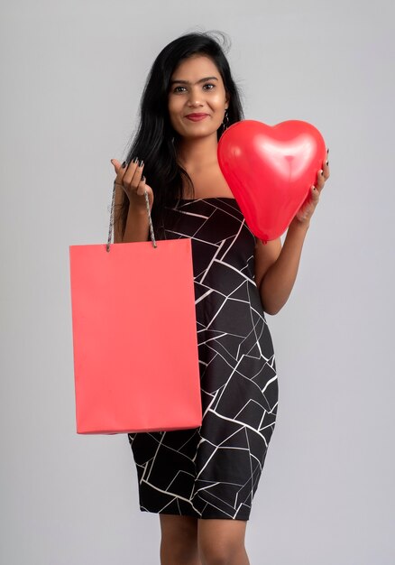 Hermosa joven posando con bolsas de la compra y un globo sobre un fondo gris