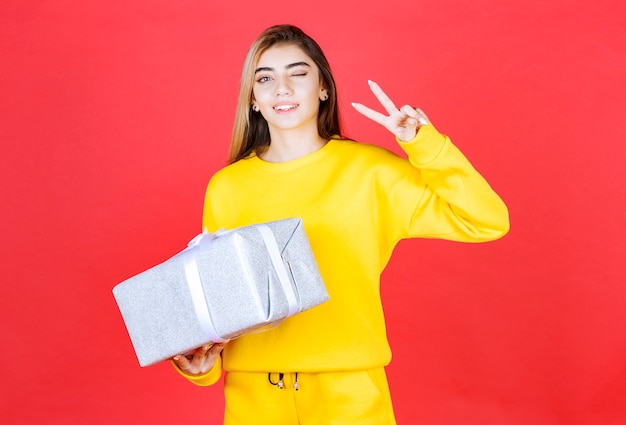 Hermosa joven posando con caja de regalo en la pared roja