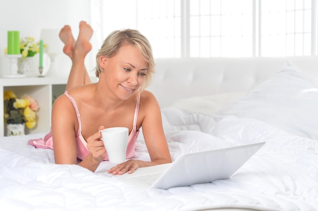 Hermosa joven posando en la cama con una laptop en casa