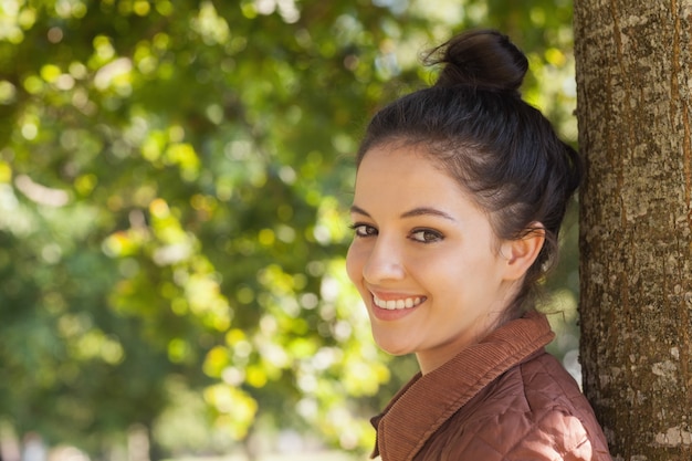 Hermosa joven posando inclinada contra un árbol