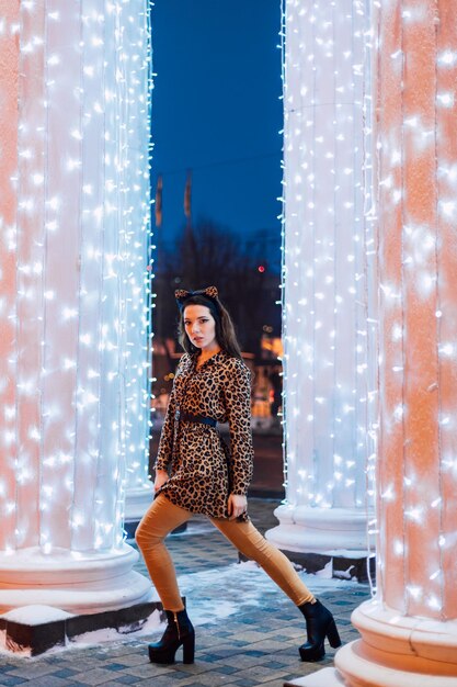 Foto hermosa joven posando con un vestido estampado de leopardo en una noche de invierno en un parque de la ciudad