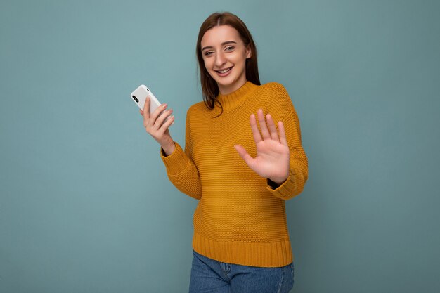 Hermosa joven positiva vistiendo un suéter naranja poising aislado sobre fondo azul.