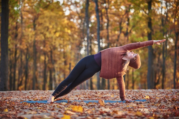 Hermosa joven practica asana de yoga de curva lateral Vasishthasana en la terraza de madera en el parque de otoño