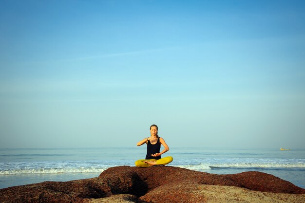 Hermosa joven practicando yoga y ejercicios de estiramiento en la playa del océano de verano.