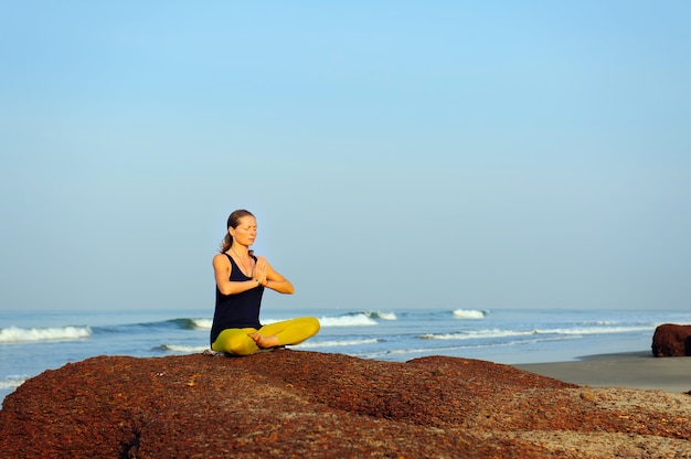 Hermosa joven practicando yoga y ejercicios de estiramiento en la playa del océano de verano.