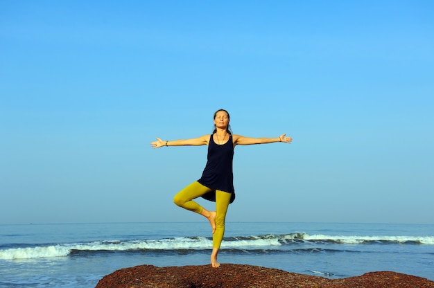 Hermosa joven practicando yoga y ejercicios de estiramiento en la playa del océano de verano