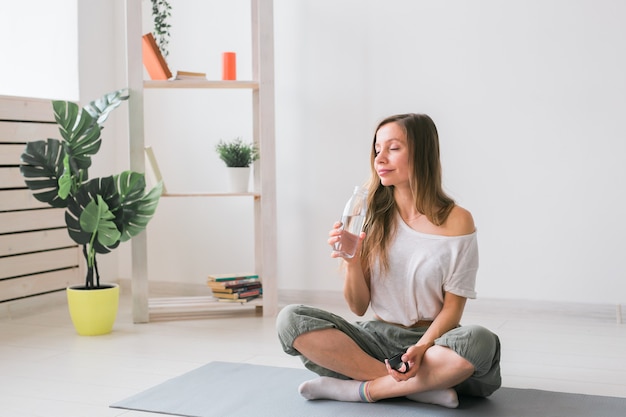 Hermosa joven practicando yoga en la estera de agua potable mientras se rompe el fitness y el estilo de vida saludable