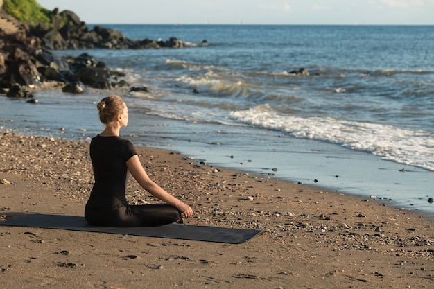 Hermosa joven practicando yoga en la playa de arena