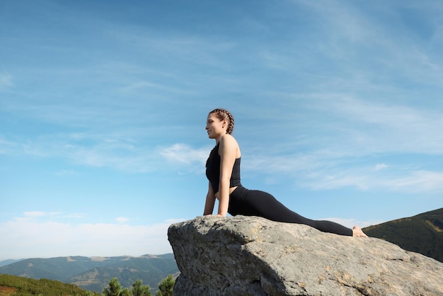 Hermosa joven practicando yoga en roca en las montañas