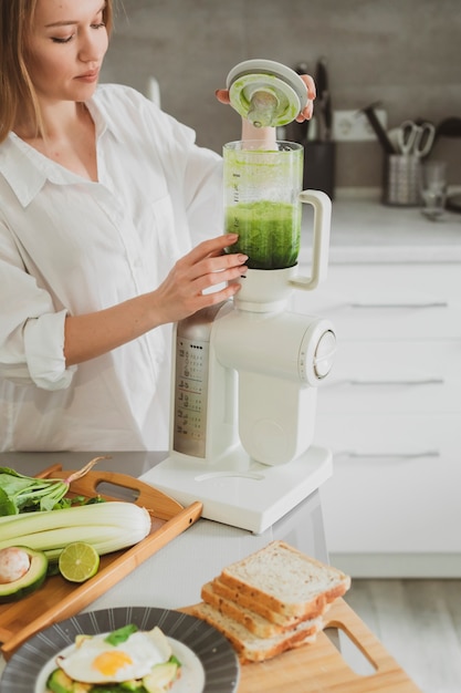 Hermosa joven preparando un batido verde saludable en su cocina