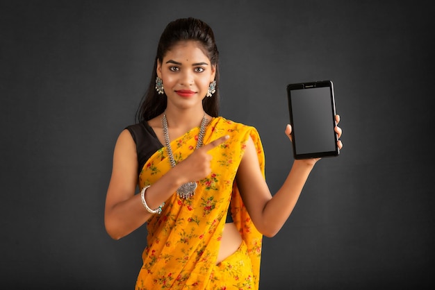 Hermosa joven que muestra una pantalla en blanco de un teléfono inteligente o teléfono móvil o tableta