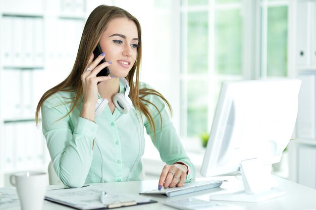 Hermosa joven que trabaja con la computadora mientras habla por teléfono