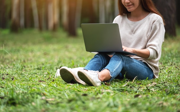 Una hermosa joven que trabaja y escribe en el teclado de una computadora portátil mientras está sentada en el parque