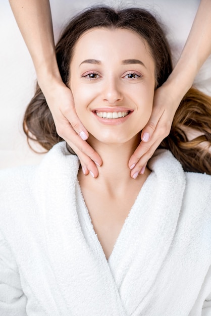 Hermosa joven recibiendo masaje facial acostado en el sofá. Vista superior centrada en la cara.