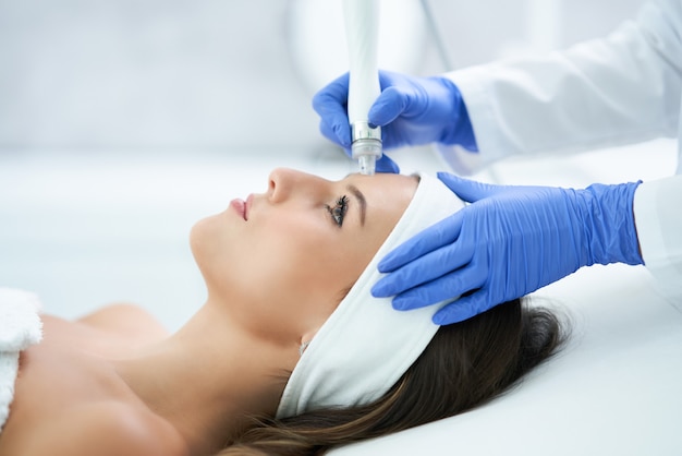 Hermosa joven recibiendo un tratamiento facial en el salón de belleza.