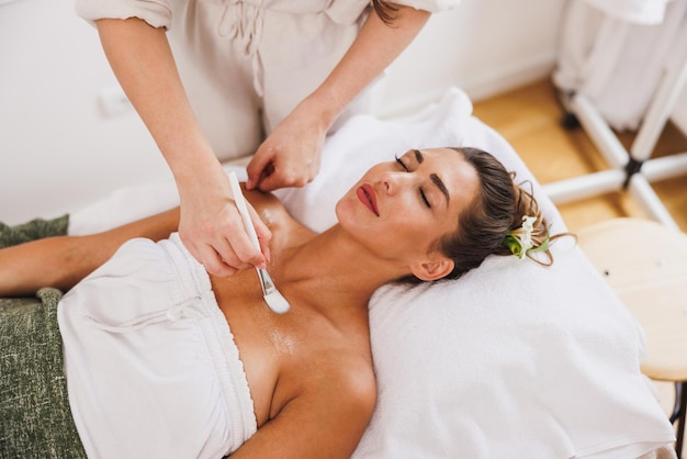 Hermosa joven recibiendo un tratamiento de mascarilla hidratante en la zona del escote en el salón de belleza.